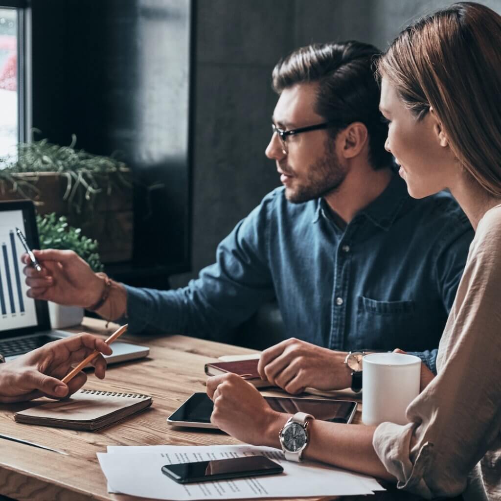 Three individuals seated at a table with a laptop and papers, discussing matters related to Capital Premium Financing.