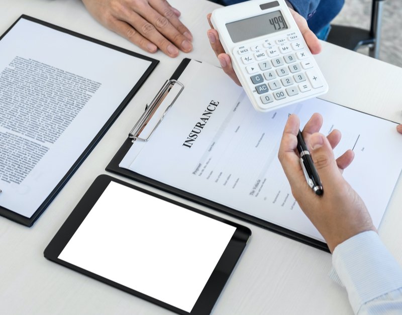 Business professionals from Capital Premium Financing signing documents and using a calculator in a collaborative office setting.