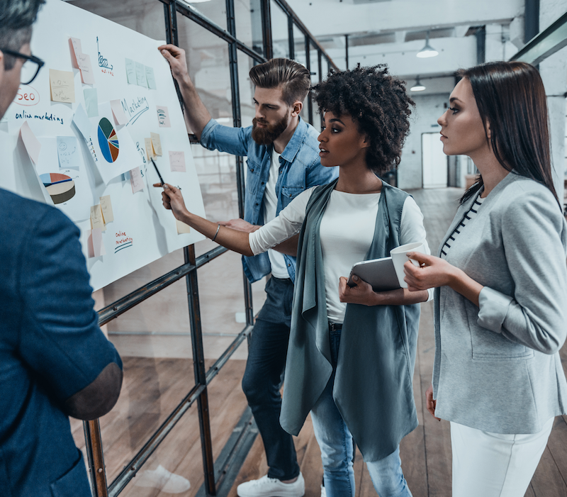 Business professionals discussing strategies around a whiteboard at a Capital Premium Financing meeting.