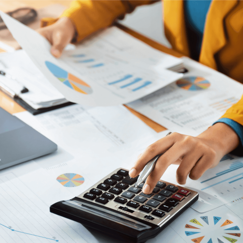 A person calculates on a desk cluttered with papers and graphs, representing financial analysis at Capital Premium Financing.
