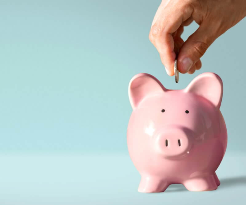 A person inserting a coin into a piggy bank, symbolizing savings and financial planning with Capital Premium Financing.