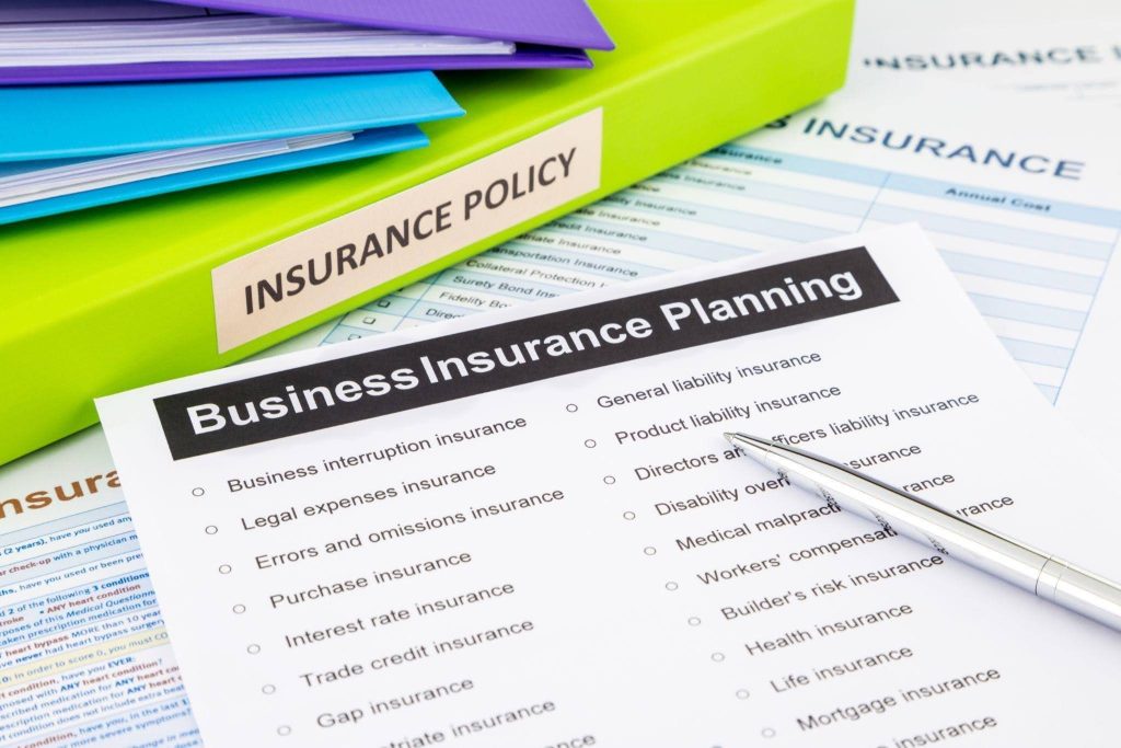 A pen rests on the paper and a green binder labeled Insurance Policy is nearby