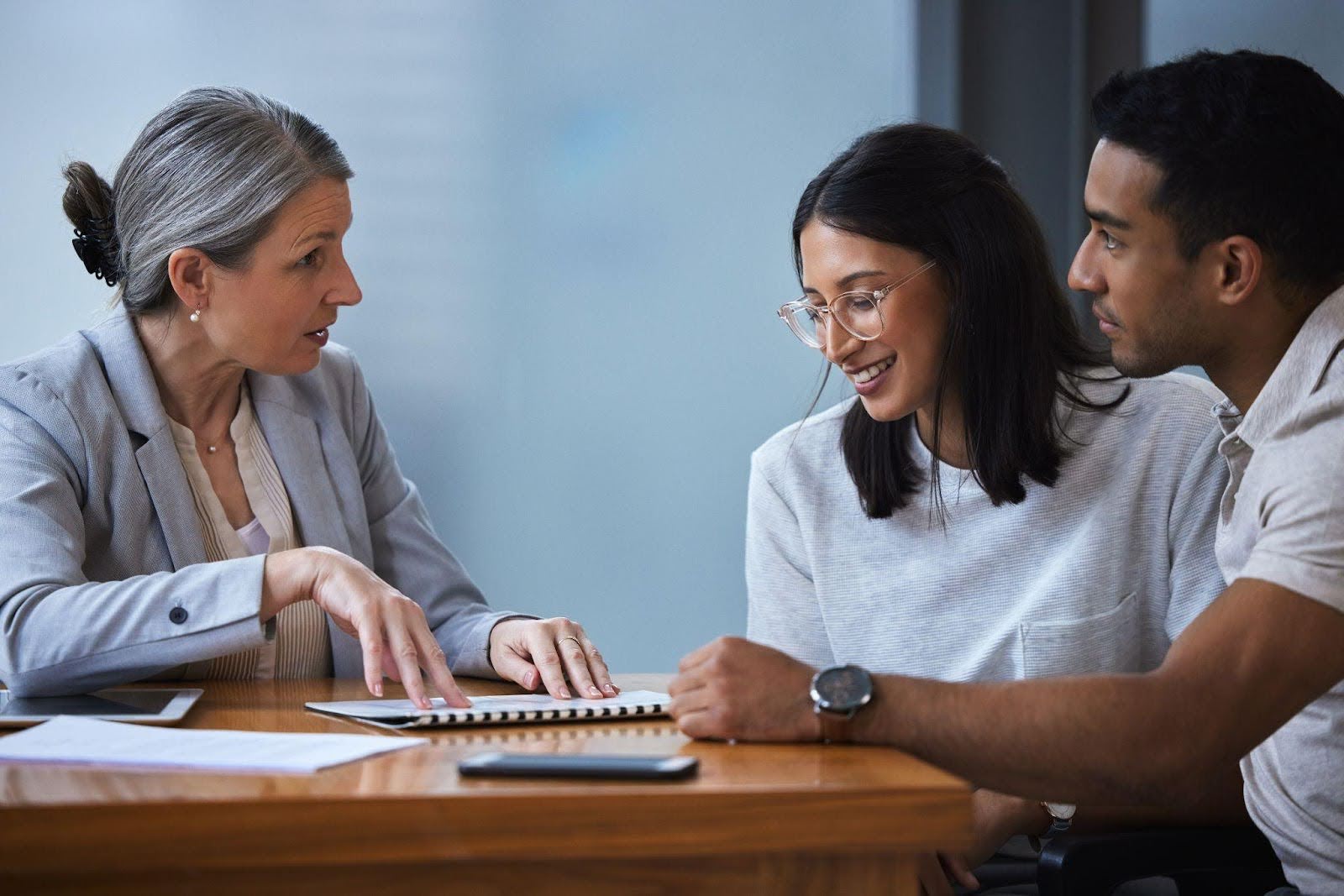A woman and two men discuss while using a laptop at a table