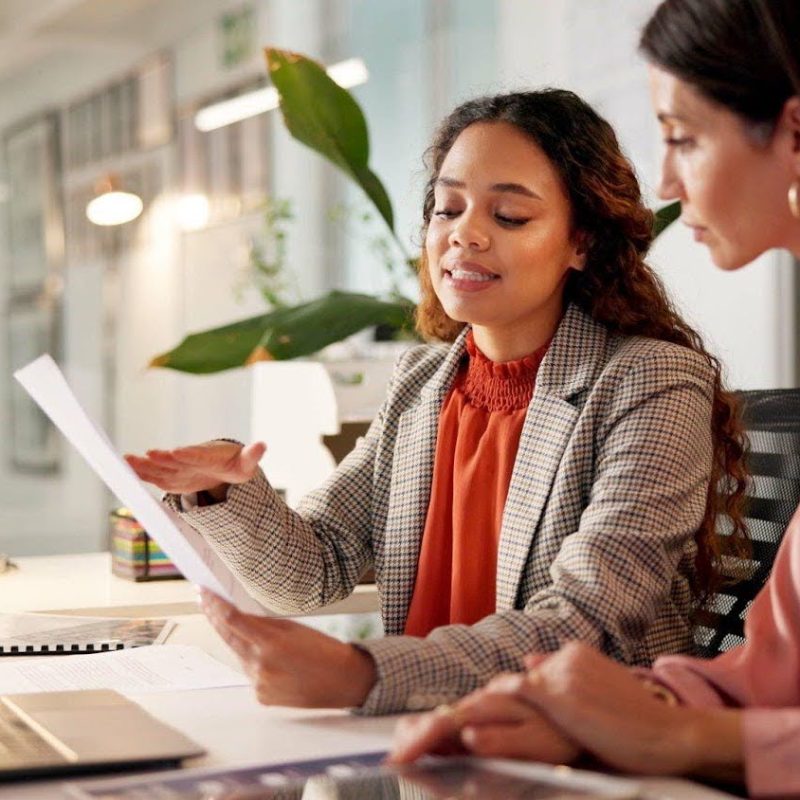 Two women work together on paperwork at a desk in an office