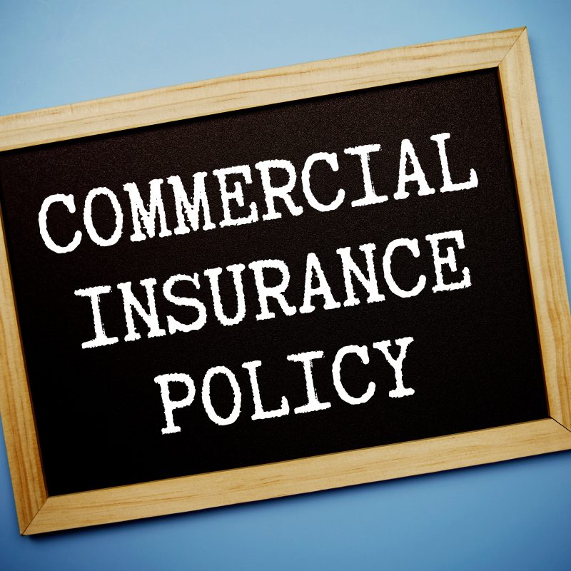 A blackboard with "Commercial Insurance Policy" written in white uppercase letters is framed with light wood against a blue background, conveying professionalism.