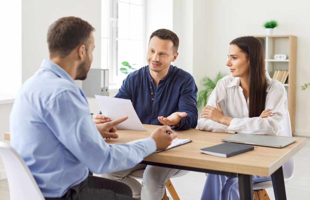 Three people discussing around a table in a modern office setting.
