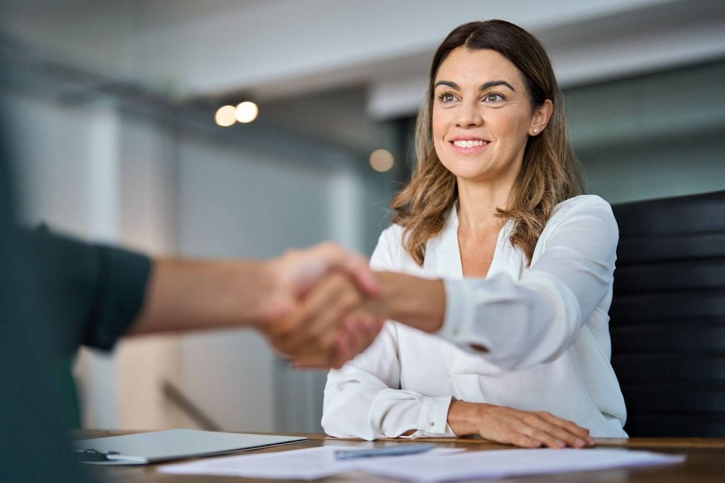 A woman and a man shake hands at a desk symbolizing a partnership