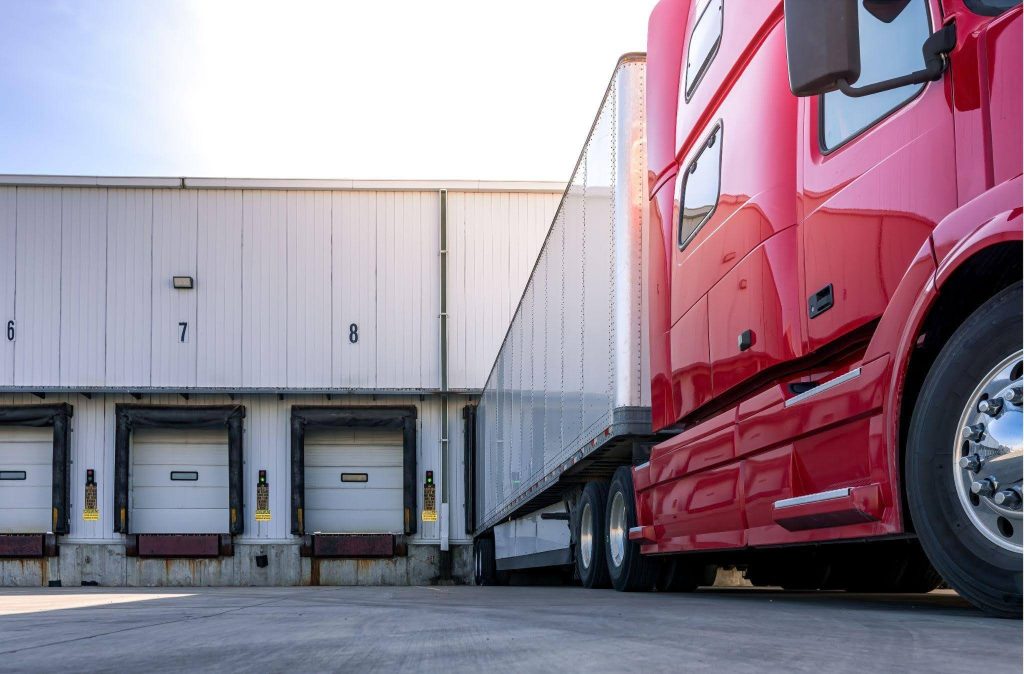 A red semi truck parked in front of a large warehouse showcasing its size and industrial setting