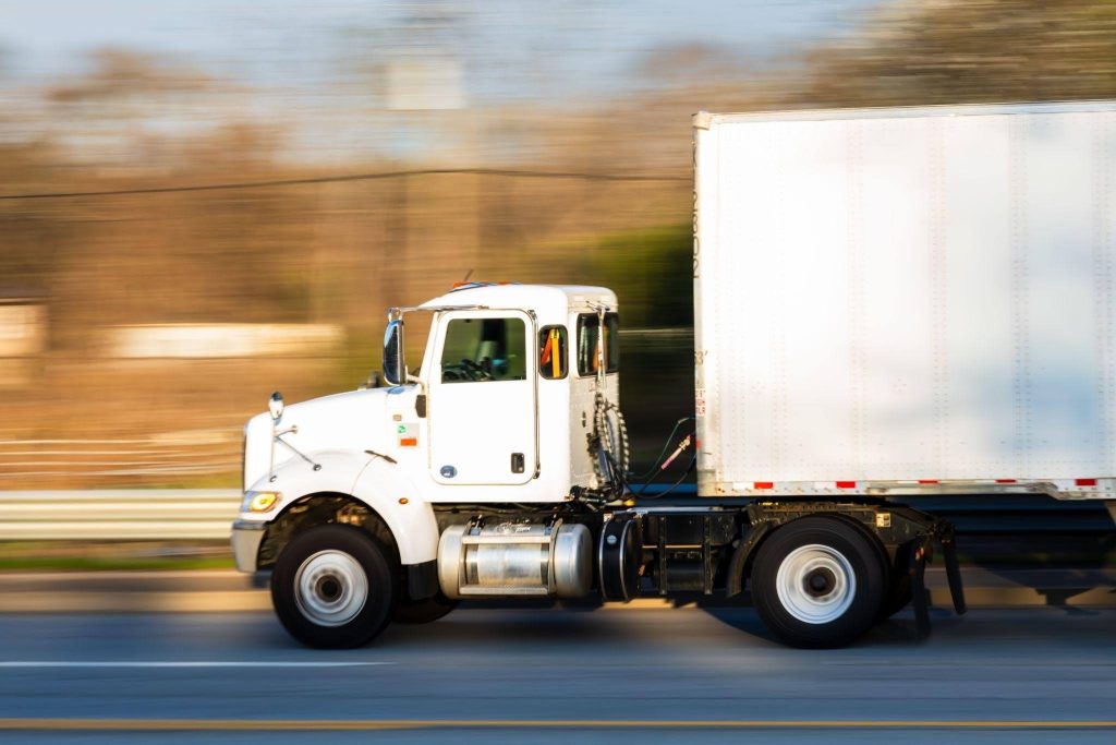A white truck traveling down a paved road with trees lining the sides