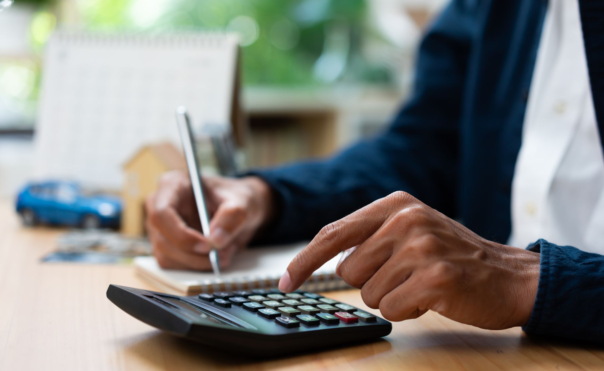 A close-up of a person using a calculator and writing in a notebook at a desk.